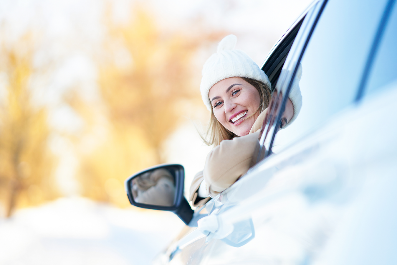 smiling woman in a hat looking outside her driver side window 